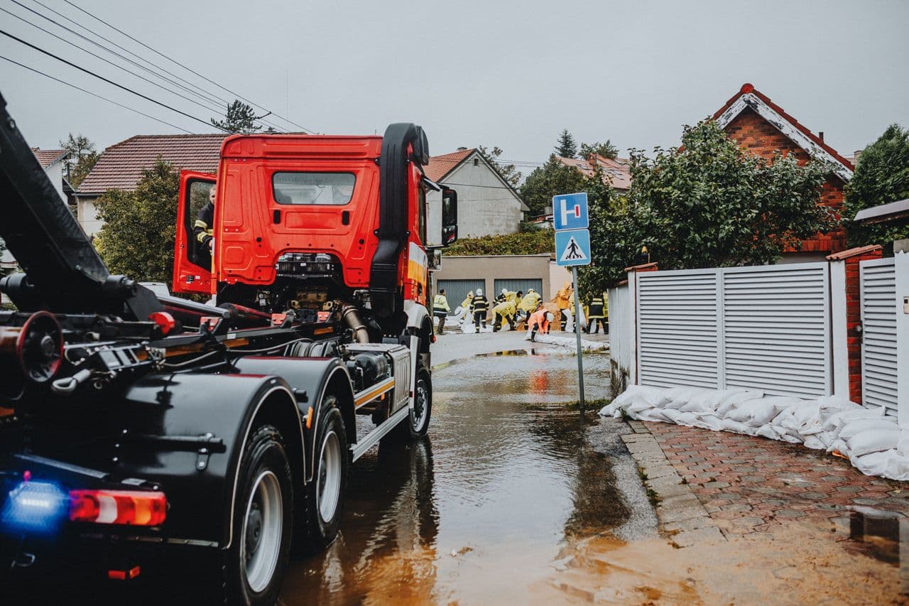 Emergency crews laying sandbags on a flooded residential street beside a red truck