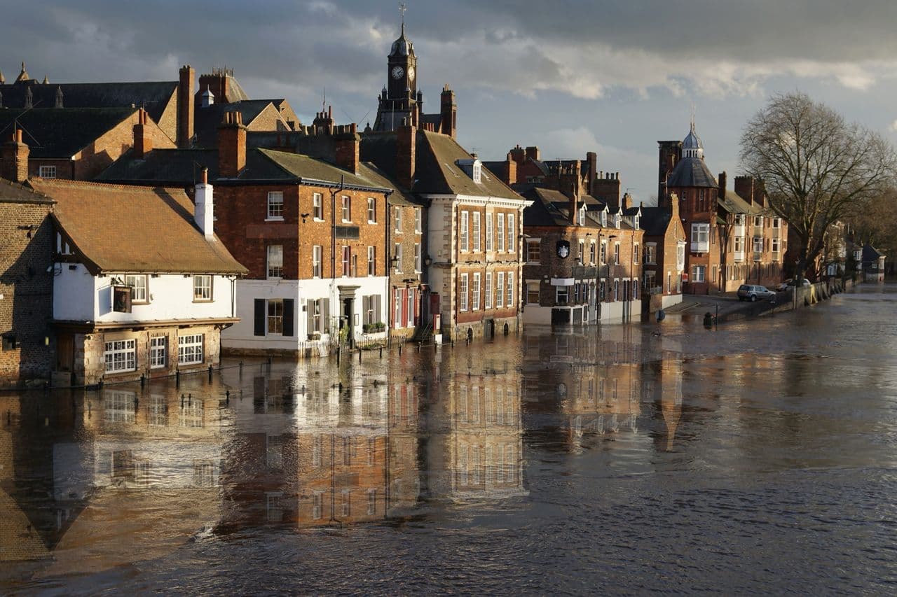 Riverside town buildings and a clock tower reflected in high floodwater