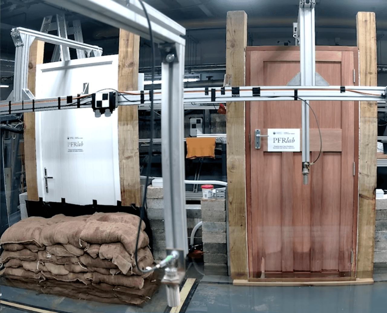 Two doors undergoing flood testing in a laboratory with PFRlab signs, featuring sandbags and testing equipment
